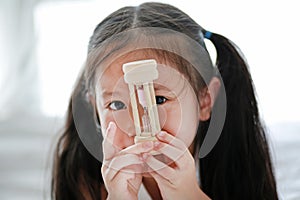 Close up little Asian girl holding sandglass in hand with looking through camera. Waiting times with hourglass