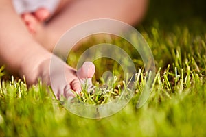 Close-up of little baby feet on green grass outdoors in the city park.