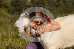 Close Up Of Little Baby Girl Hugs Goat On Meadow In Summer