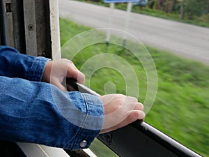 Close up of little baby`s hands holding on a frame of an opened window on a traveling train