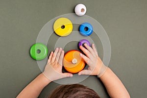 Close up of little baby wearing pajamas playing with wooden toy pyramid on green background . Natural eco toys concept.