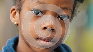 Close-up little beautiful afro girl in park schoolgirl seriously looking at camera. Portrait of brown eyes african