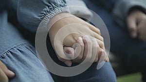 Close-up of little boy and girl holding hands. Unrecognizable Caucasian couple of children sitting outdoors. Unity and