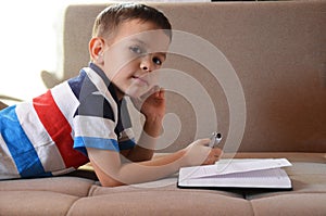 Close up little boy hand writing on paper, Kid writing on sofa in living room, student child boy holding colour pencil learning ho