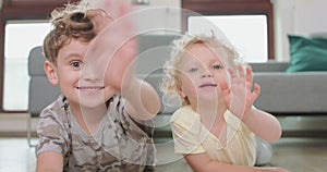 Close up of a little boy and a little girl, who are laying on the floor and waving hands, looking to the camera Grey