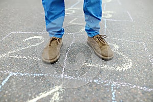 Close-up of little boy`s legs and hopscotch drawn on asphalt. Child playing hopscotch game on playground on spring day