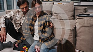 Close up, a little brunette girl in pink clothes draws lying on the floor her parents look at her a brunette man with