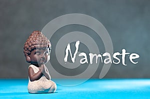 Close-up of little buddha meditating, focus on arms in Namaste gesture and text namaste - yoga and zen concept