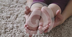Close-up of little Caucasian baby`s feet hold by female hands. Tenderness, joy of motherhood, happiness, lifestyle