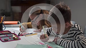 Close-up of little Caucasian boy sitting with his classmate, writing in exercise book, and talking. Two schoolmates