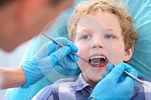 Close-up of little Caucasian curly boy opening his mouth wide during inspection of oral cavity by dentist.