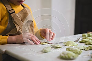 Close-up little child hands stuffing a sculpting dumplings, standing at floured table in the rustic kitchen