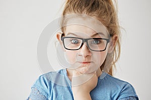 Close up of little cute girl with big blue eyes and light hair looking at camera with angry face expression and raised