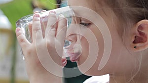 Close-up of a little cute girl drinking pure water from a glass