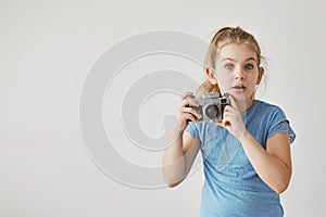 Close up of little cute girl with light hair in blue t-shirt looking in camera with surprised face expression, holding