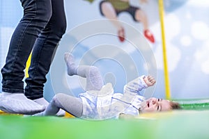 Close up of little cute toddler girl in a dress with mother jumping on a trampoline and laughing. on the children`s