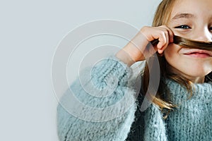 Close up of a little girl in a blue sweater joking around, making fake mustache
