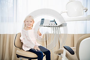 A close-up of a little girl in a dentist office showing thumbs up. Children visiting dentists concept. Tooth healthcare