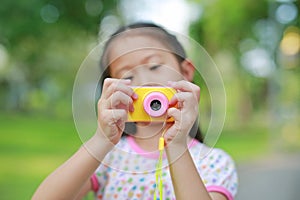 Close-up little girl with digital camera toy in the garden outdoor. Focus at camera in hands