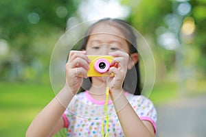 Close-up little girl with digital camera toy in the garden outdoor. Focus at camera in hands