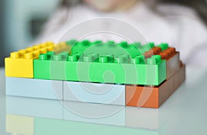 Close up of little girl hands building with plastic colorful blocks construction at home.
