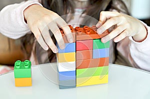 Close up of little girl hands building with plastic colorful blocks construction at home.