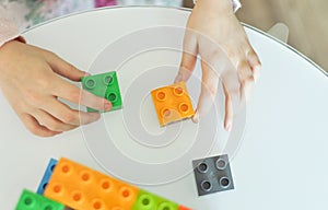 Close up of little girl hands building with plastic colorful blocks construction at home