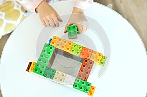 Close up of little girl hands building with plastic colorful blocks construction at home