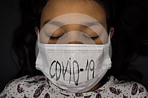 Close up little girl with her eyes closed wearing surgical masks with word covid19 written on black