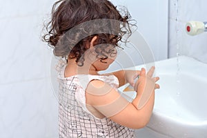 Little cute baby girl cleaning her teeth with toothbrush in the bathroom.