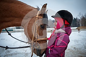 Close up of a little girl horse rider smiling and looking to the horse eyes.