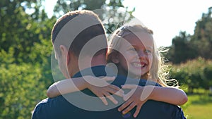 Close up of little girl laughing hugging her dad in park. Family concept. Rear of male parent holding his small child on