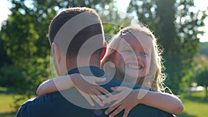 Close up of little girl laughing hugging her dad in park. Family concept. Rear of male parent holding his small child on