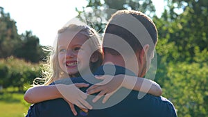 Close up of little girl laughing hugging her dad in park. Family concept. Rear of male parent holding his small child on