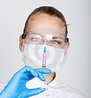 Close-up little girl in a medical dress and gloves holding a syringe