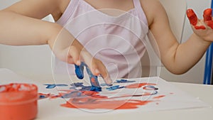 Close-up of a little girl`s hand, drawing on paper with bright colors, dipping her fingers in cans of paint.