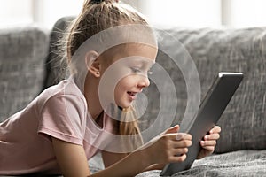 Close up little girl using computer tablet, lying on couch