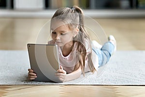 Close up little girl using computer tablet, lying on floor