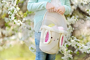 Close-up of little girls hands holding cute Easter basket in blooming cherry garden on beautiful spring day. Kid hunting for