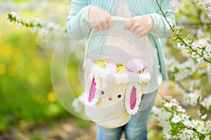 Close-up of little girls hands holding cute Easter basket in blooming cherry garden on beautiful spring day. Kid hunting for