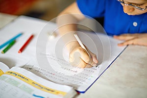 Close-up of little kid boy with glasses at home making homework, writing letters with colorful pens.