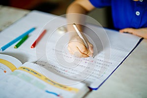 Close-up of little kid boy with glasses at home making homework, writing letters with colorful pens. Little child doing