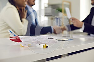 Close up of little model airplane on table on background of happy couple in travel agency office.