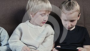 Close up of little smiling brothers playing the games on mobile phone at home.