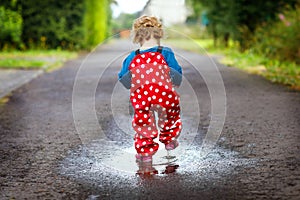 Close-up of little toddler girl wearing rain boots and trousers and walking during sleet, rain on cold day. Baby child