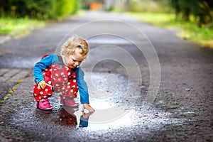 Close-up of little toddler girl wearing rain boots and trousers and walking during sleet, rain on cold day. Baby child