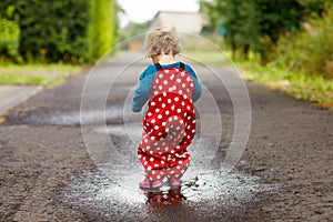 Close-up of little toddler girl wearing rain boots and trousers and walking during sleet, rain on cold day. Baby child