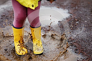 Close-up of little toddler girl wearing yellow rain boots and walking during sleet on rainy cloudy day. Cute child in