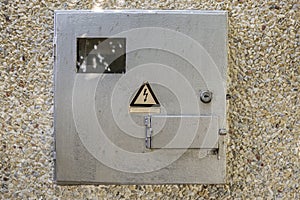 Close-up of locked electrical metal light blue meter box with warning caution sign outside on exterior house wall. Measurement