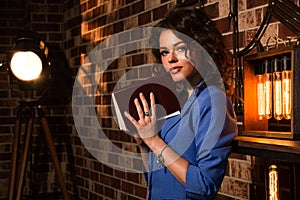 Close up. Loft. Portrait of a sexy girl in a blue jacket witk a book in her hands. Near it is a bookshelf with incandescent lamps